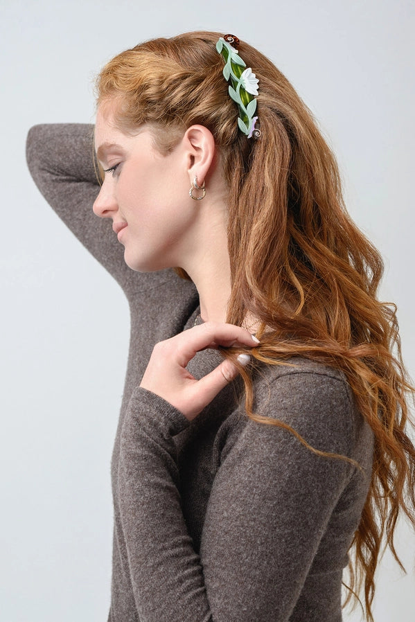 Woman with long brown hair wearing a green hair clip against a plain background