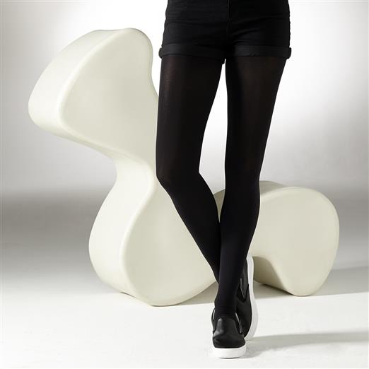 Black opaque tights shown on a model's legs, positioned against a large, off-white, abstractly shaped sculpture.