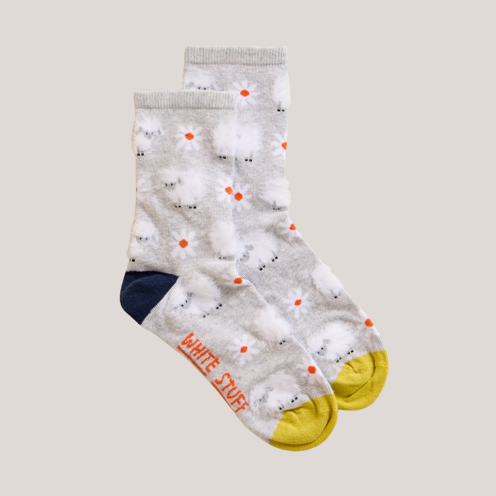 Pair of grey crew socks with a pattern of white lambs and orange daisies. Yellow and navy accents.