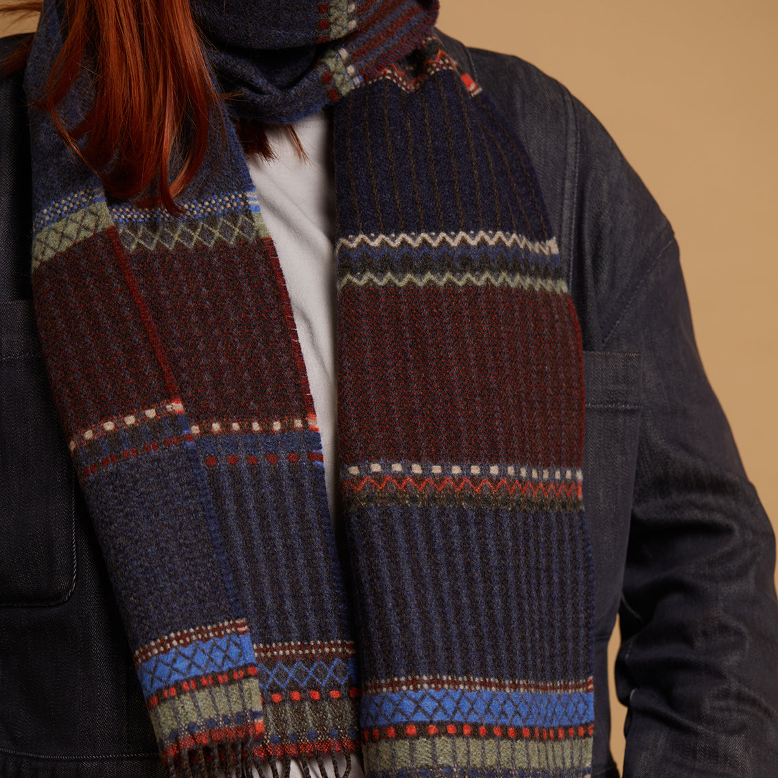 Person wearing a dark coat with a patterned scarf against a beige background