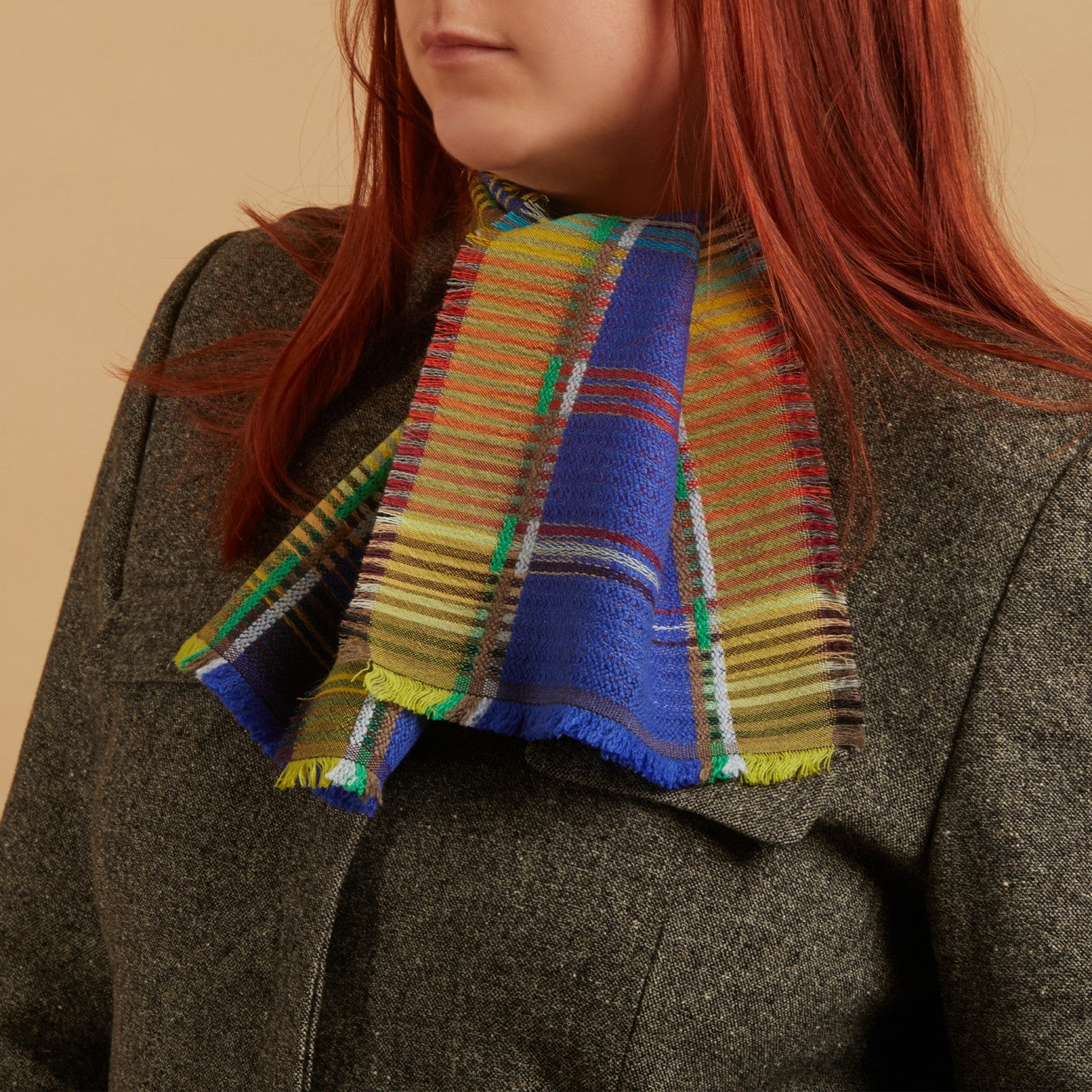 Person wearing a colorful plaid scarf with a brown coat on a beige background