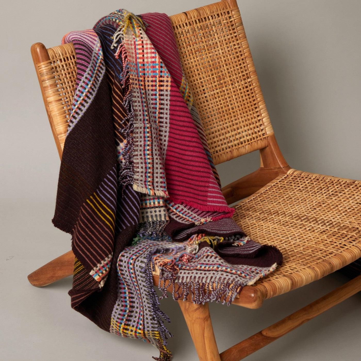 Woven blanket draped over a wicker chair against a neutral background