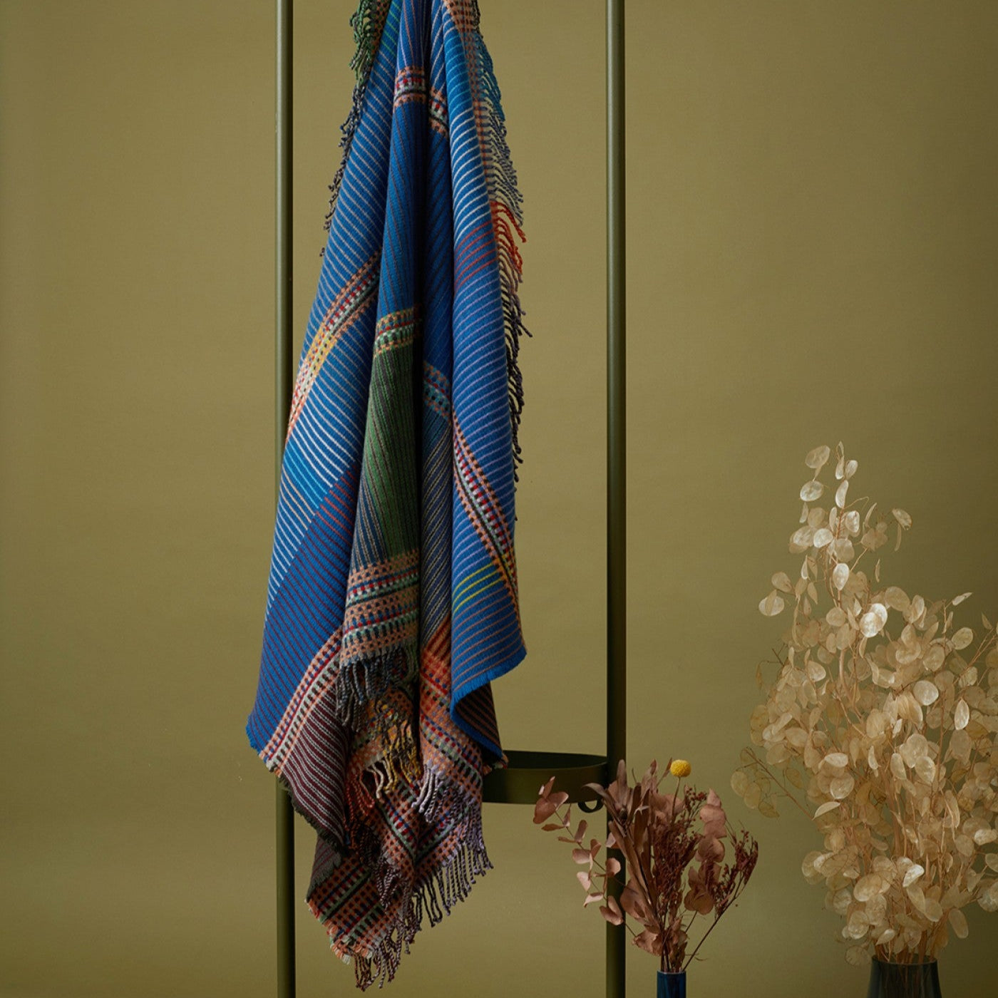 Colorful patterned towel hanging on a rack against a green wall with decorative elements.
