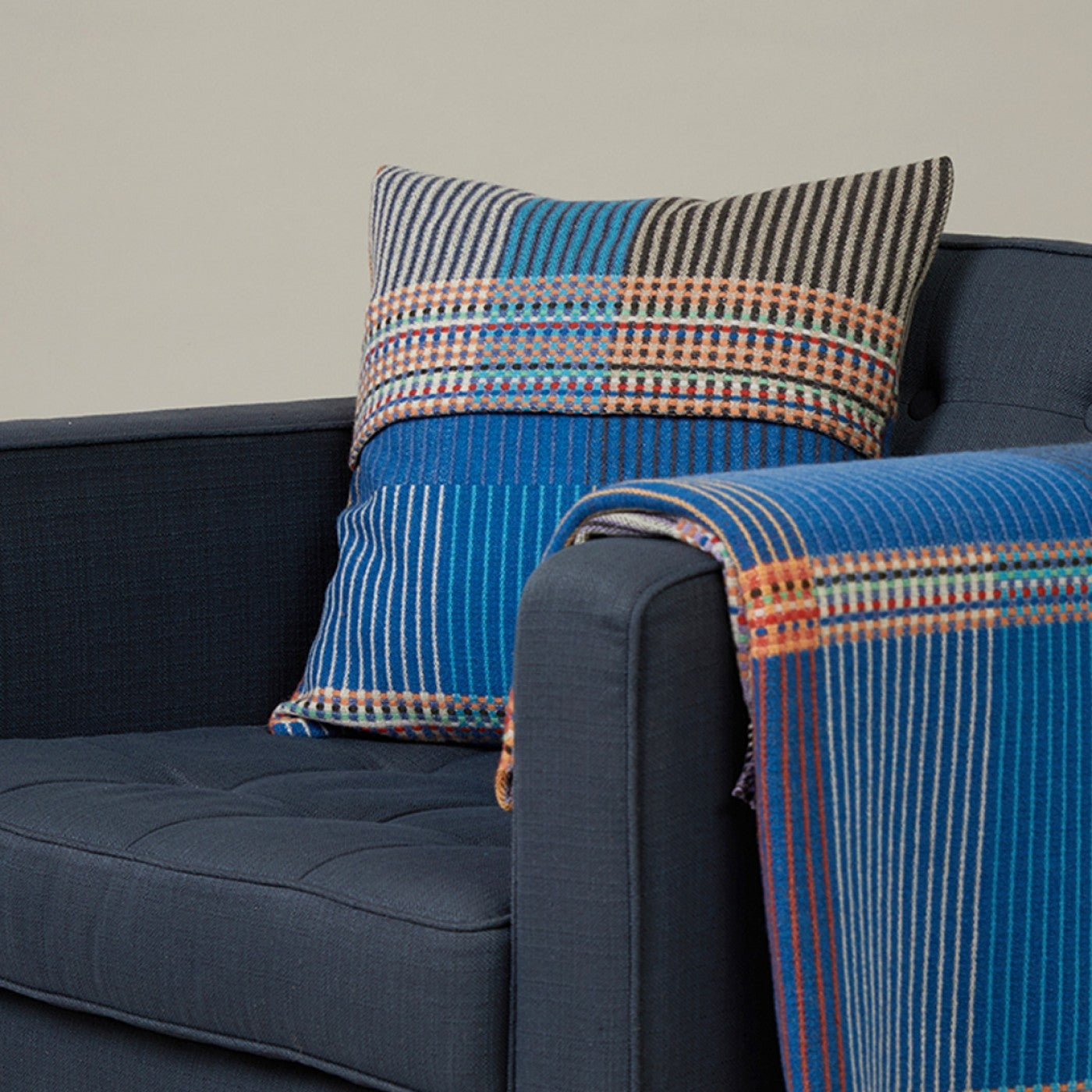 Blue plaid pillow and blanket on a dark blue sofa against a neutral background