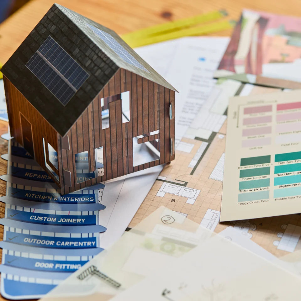 Model of a house with solar panels on a table with architectural plans and color swatches.