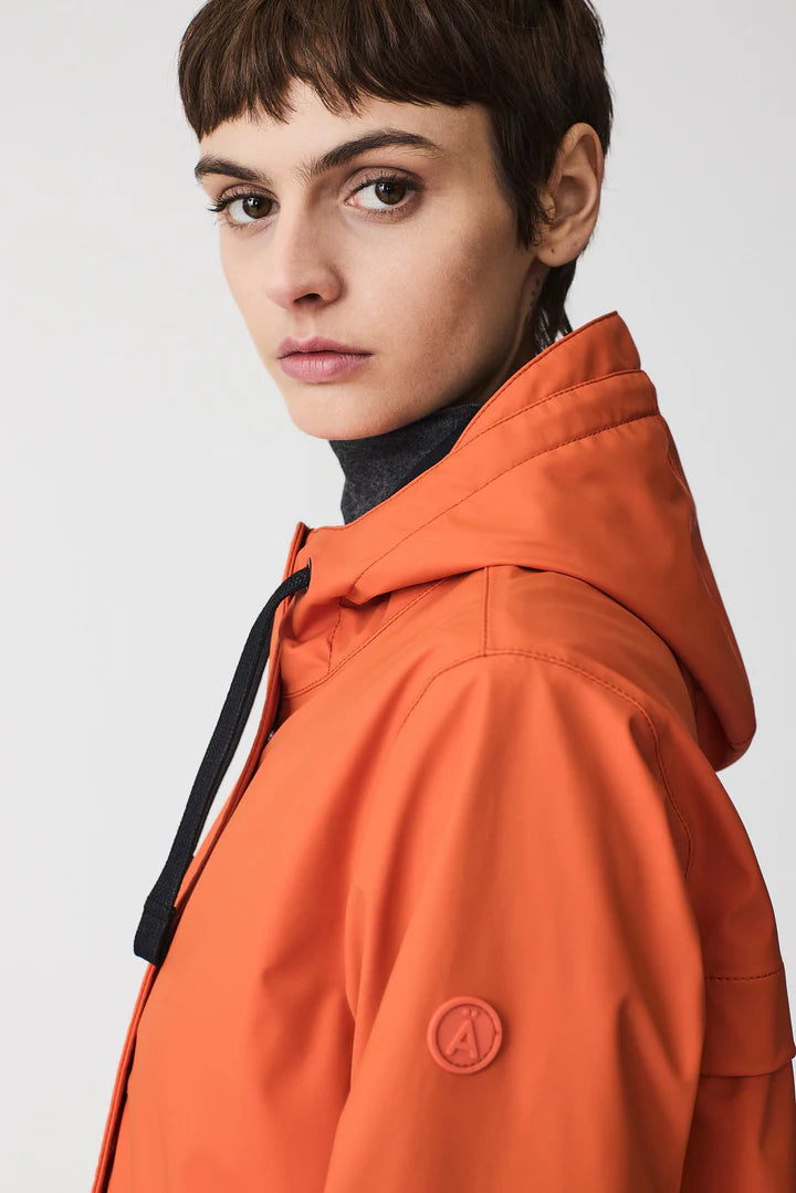 Person wearing an orange jacket with a brand logo on a white background