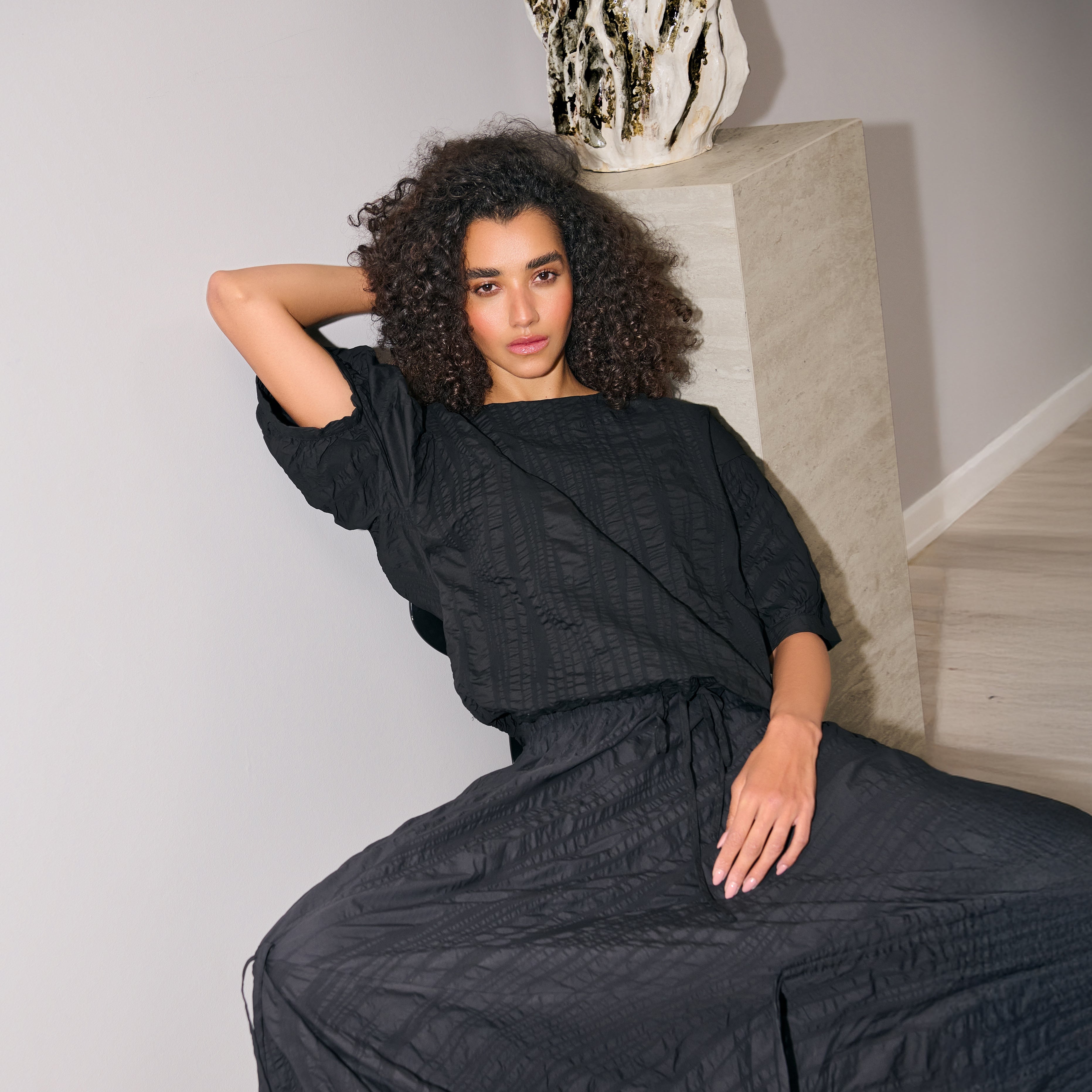 Woman wearing a black textured dress sitting on a staircase.