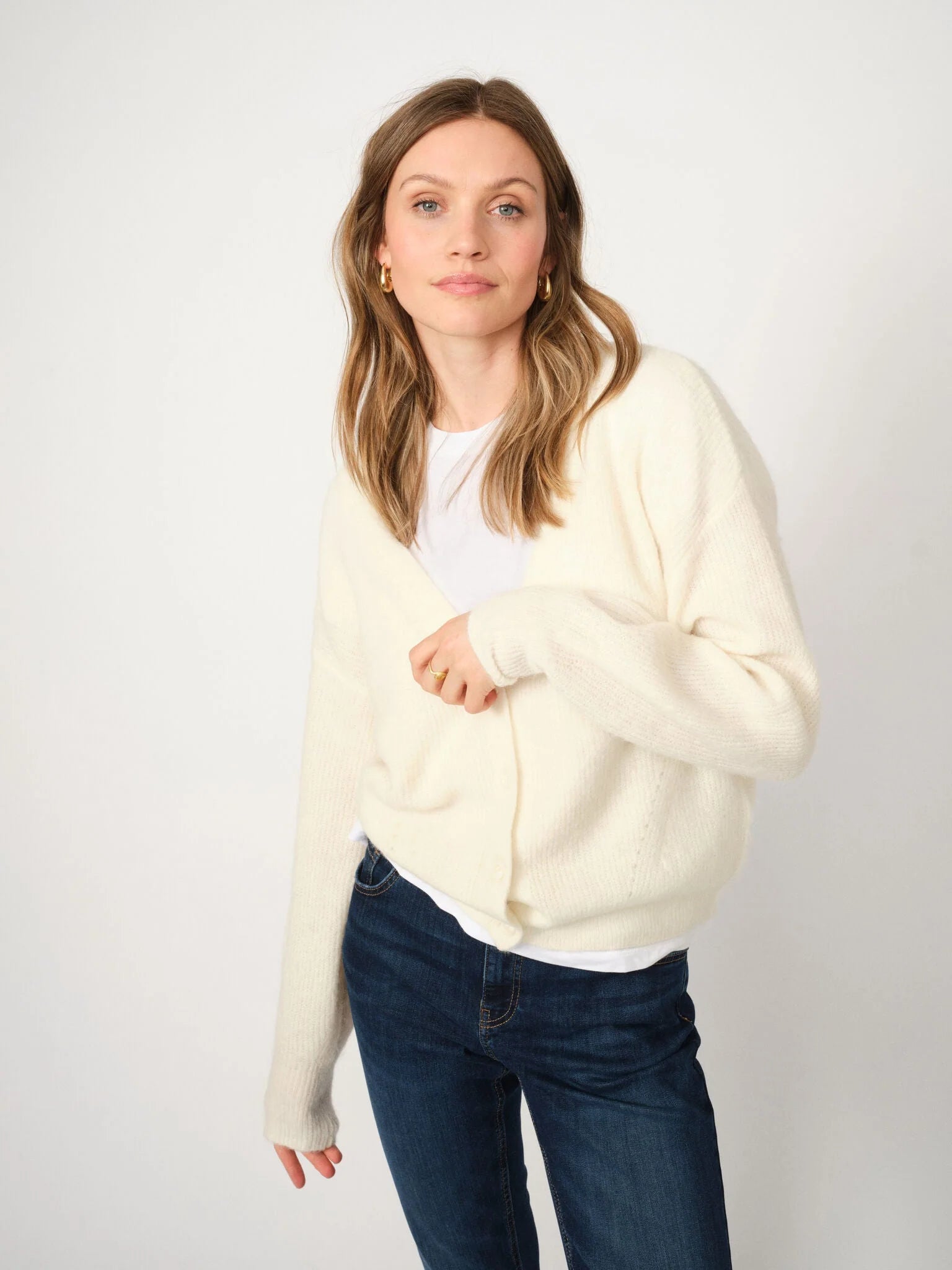 Woman wearing a cream sweater and blue jeans on a white background