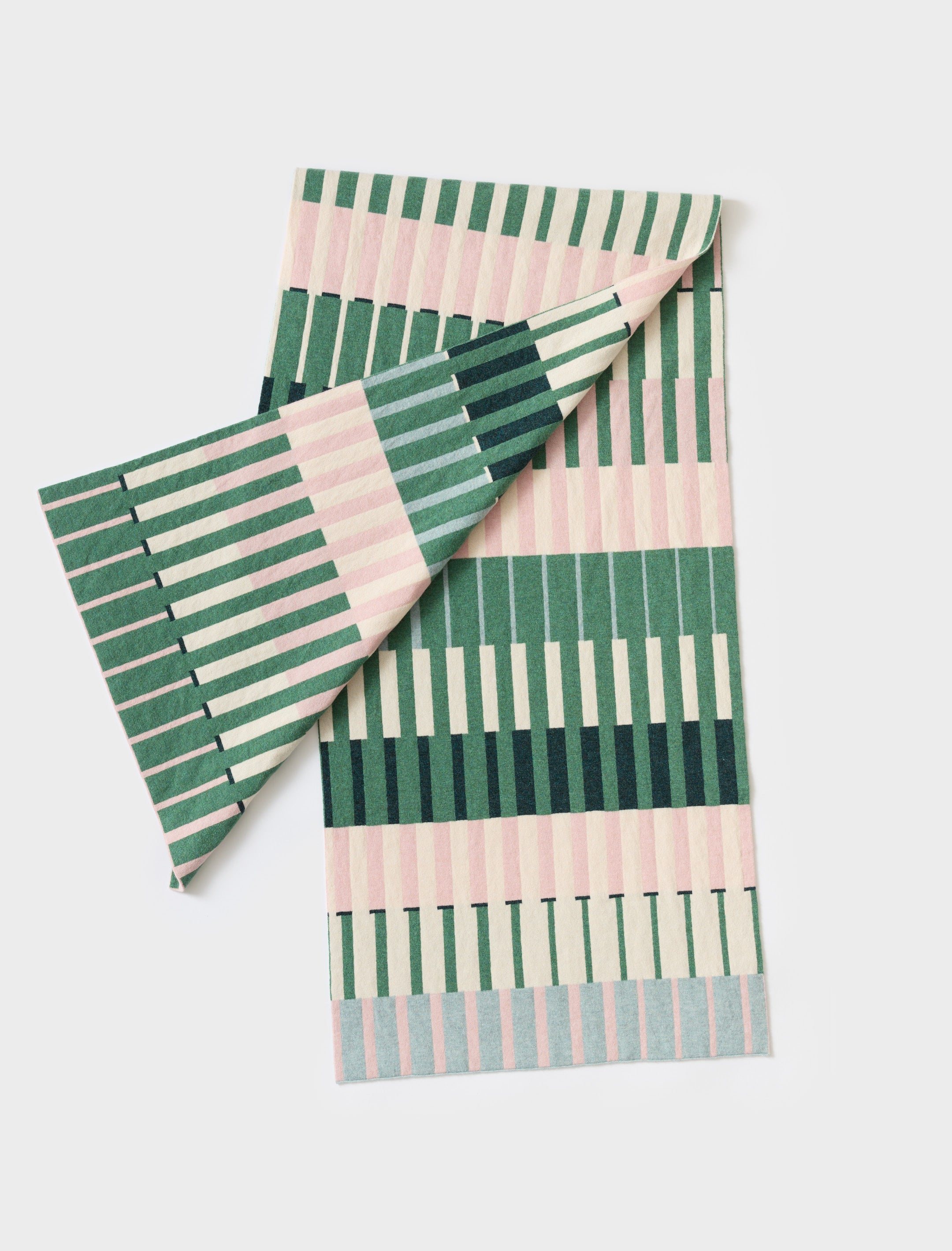Woven throw blanket with a geometric pattern in shades of green, pink, and cream.