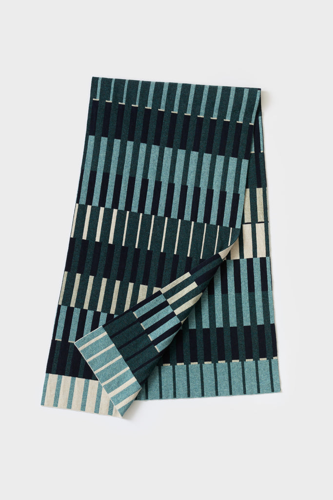 Knitted throw blanket in teal, dark green, and cream, featuring a geometric pattern of vertical stripes and rectangles.