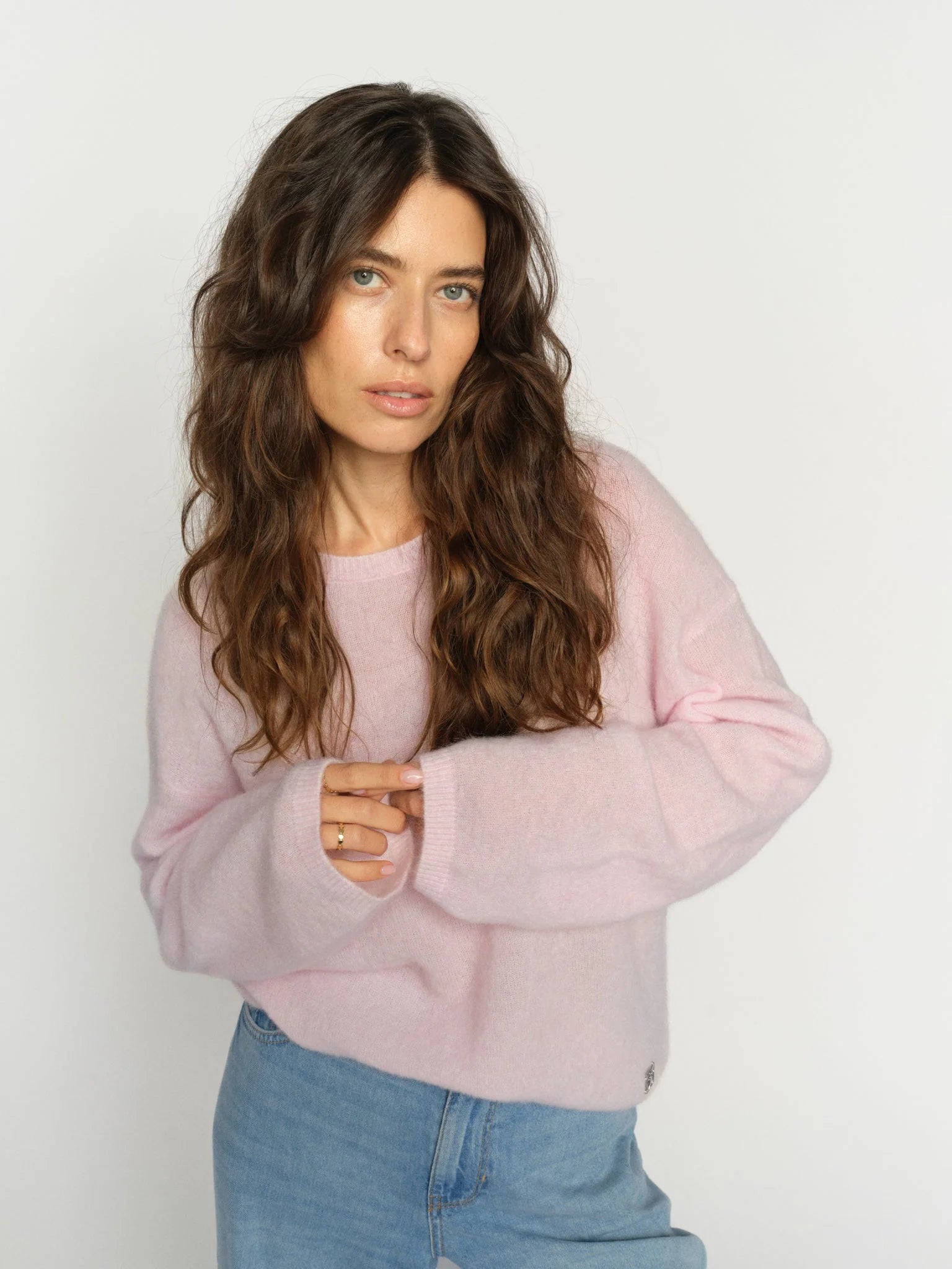Woman wearing a light pink sweater and blue jeans against a white background