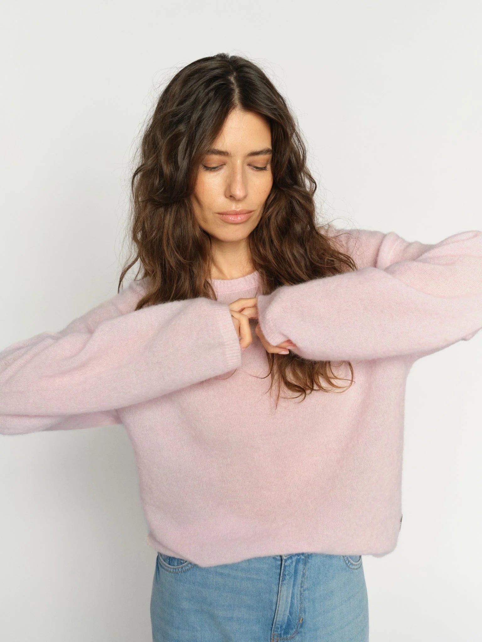 Woman wearing a light pink sweater and blue jeans against a white background
