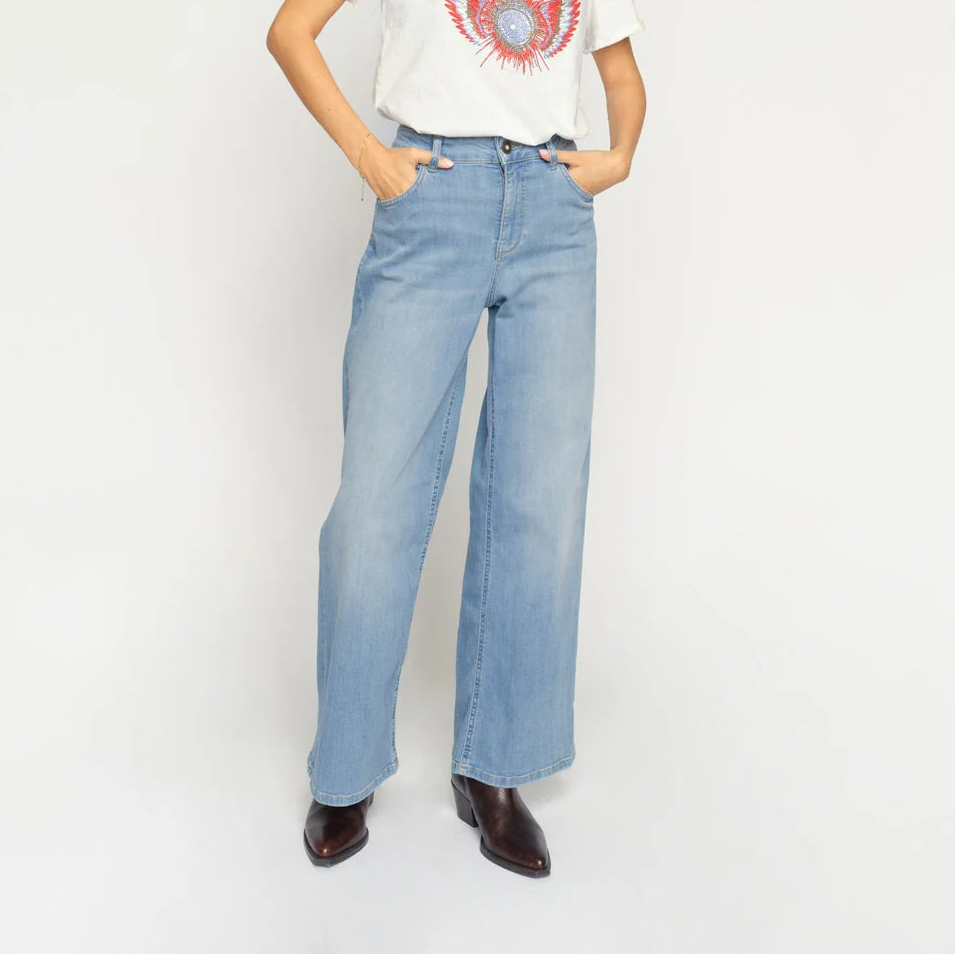 Woman wearing a white t-shirt with a graphic design and light blue jeans on a white background