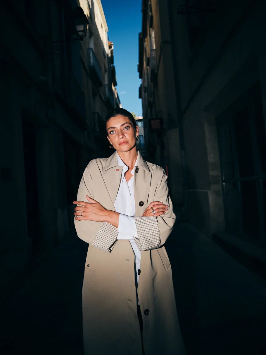 Person wearing a trench coat standing in an alleyway with a blue sky.