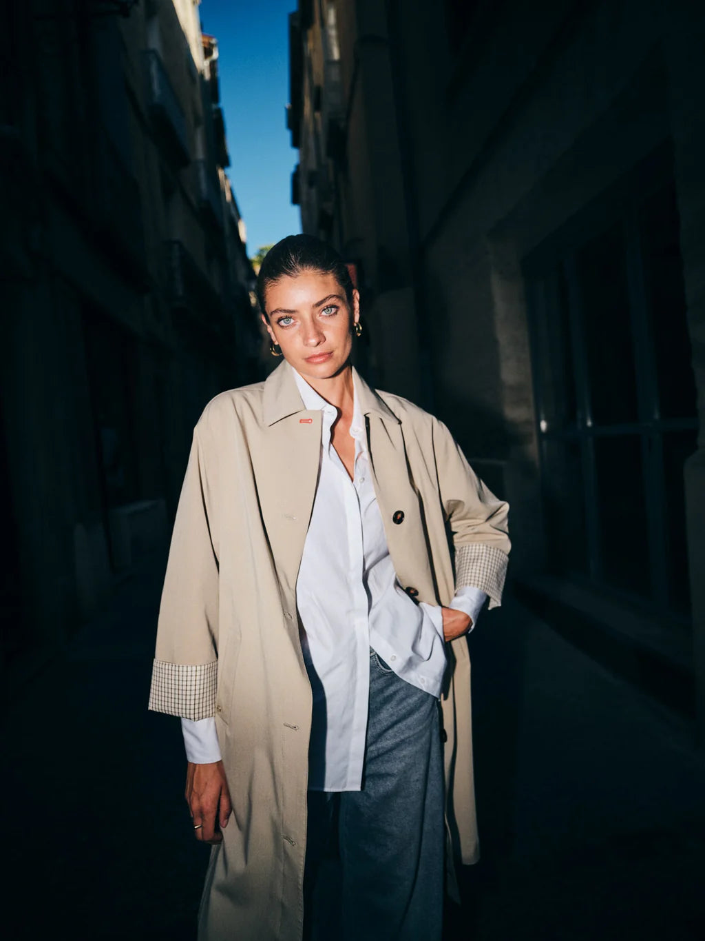 Woman in a beige coat standing in an urban alleyway