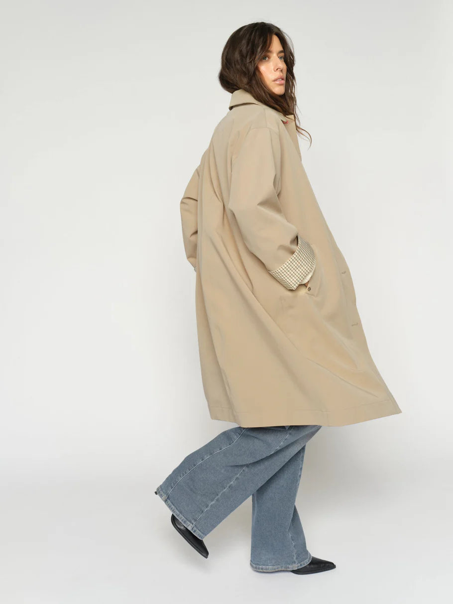 Person wearing a beige trench coat and blue jeans on a white background