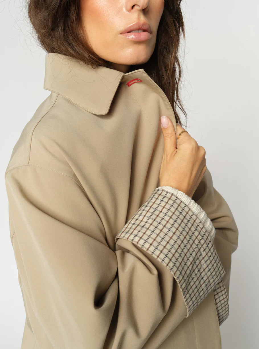 Close-up of a beige coat with plaid cuff on a plain background