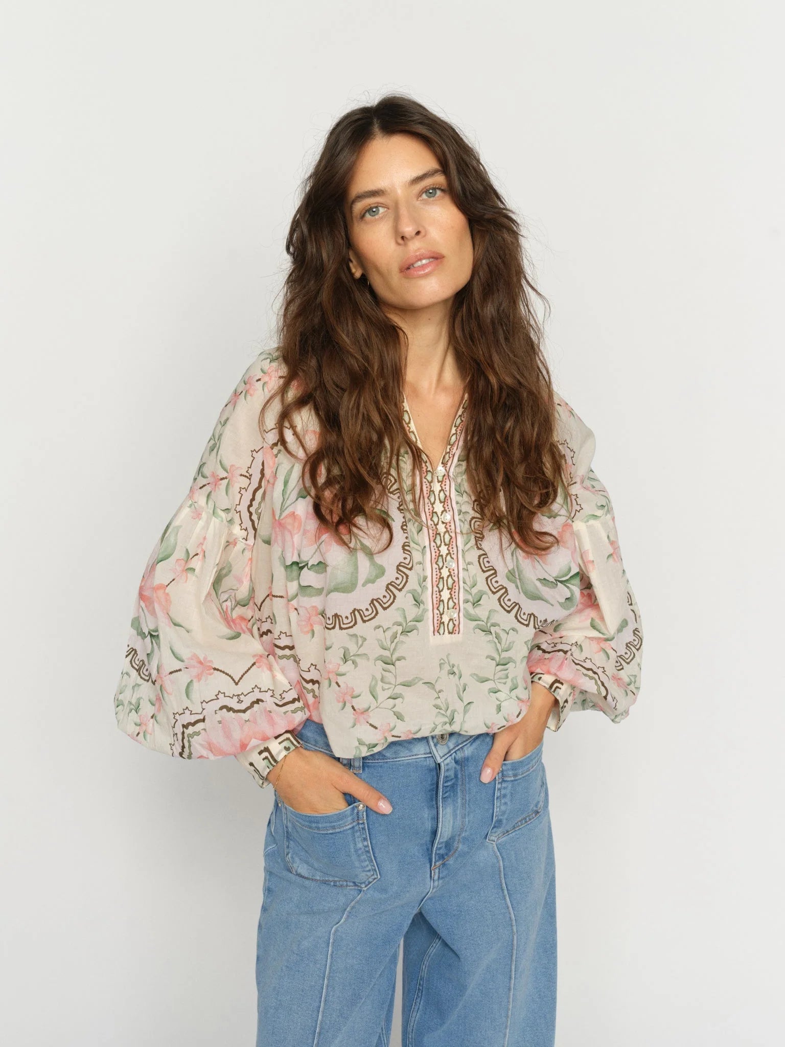 Woman wearing a floral blouse with embroidery and blue jeans on a white background