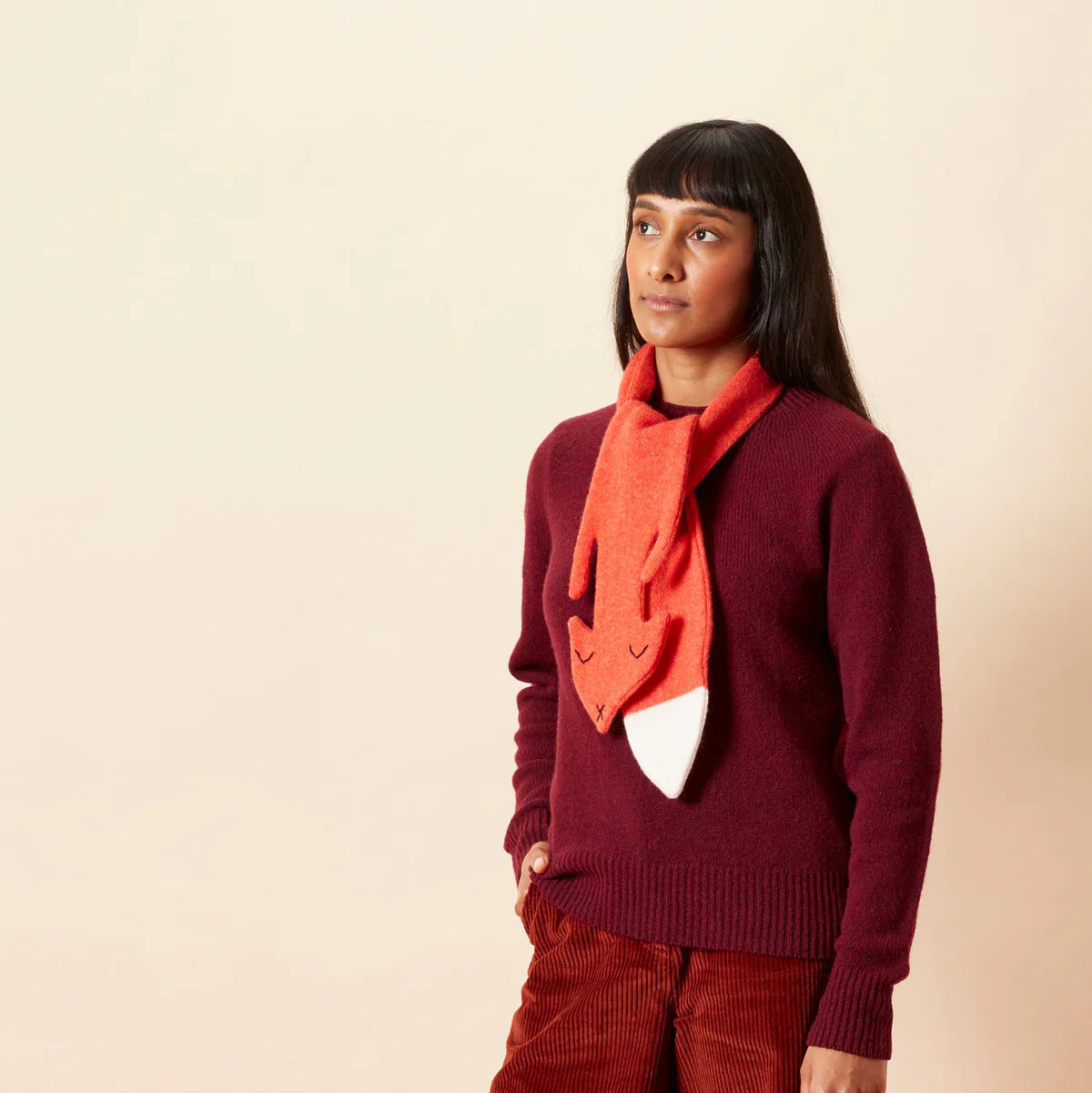 Woman wearing a burgundy sweater and red scarf with a white heart design on a beige background