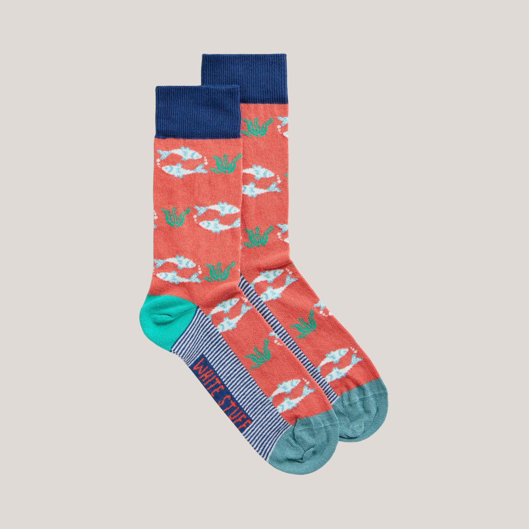 Pair of coral socks with a repeating pattern of white fish and green seaweed. Navy blue cuffs and teal ribbed cuffs.