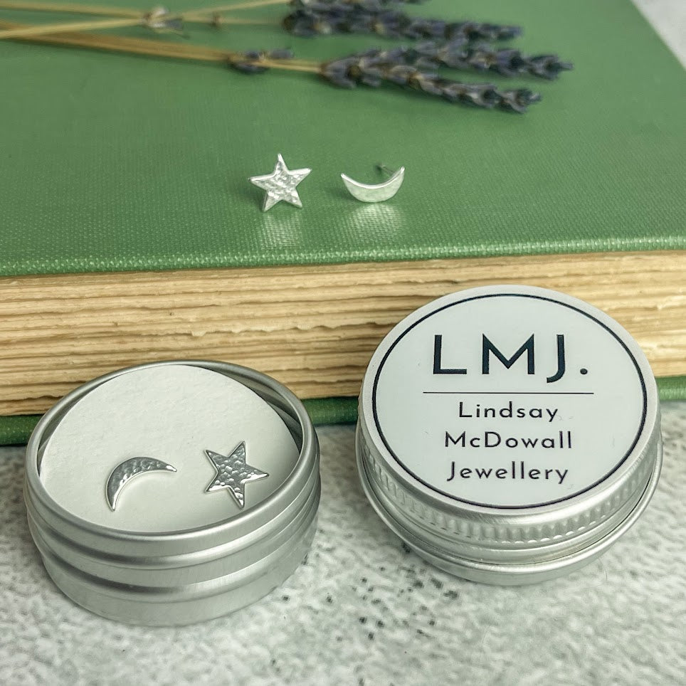 Silver star and crescent moon stud earrings in a small tin.
