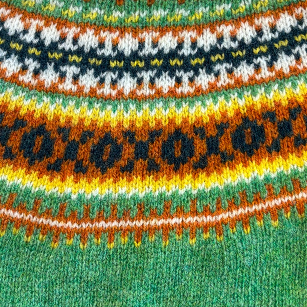 Close-up of a knitted fabric with a colorful Fair Isle pattern in greens, oranges, yellows, and blacks.