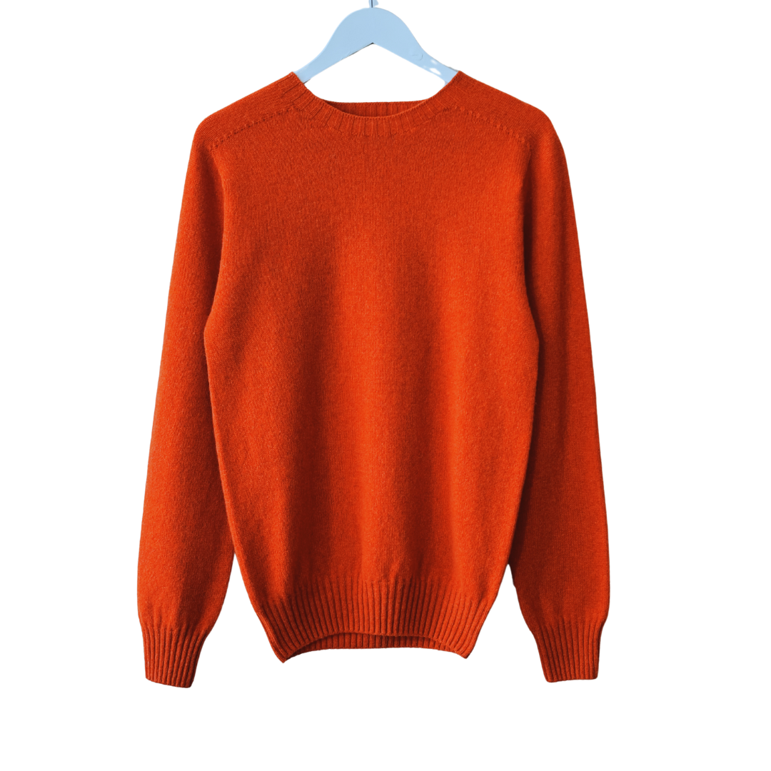 Orange crewneck sweater hanging on a light blue hanger. Long sleeves, ribbed cuffs and hem.