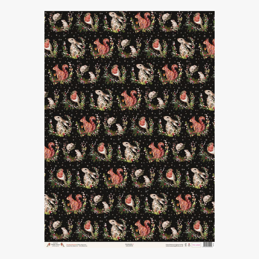 A rectangular sheet of patterned craft paper or fabric with a repeating whimsical design of rabbits, squirrels, and gnomes on a black background, shown against a light gray studio backdrop.