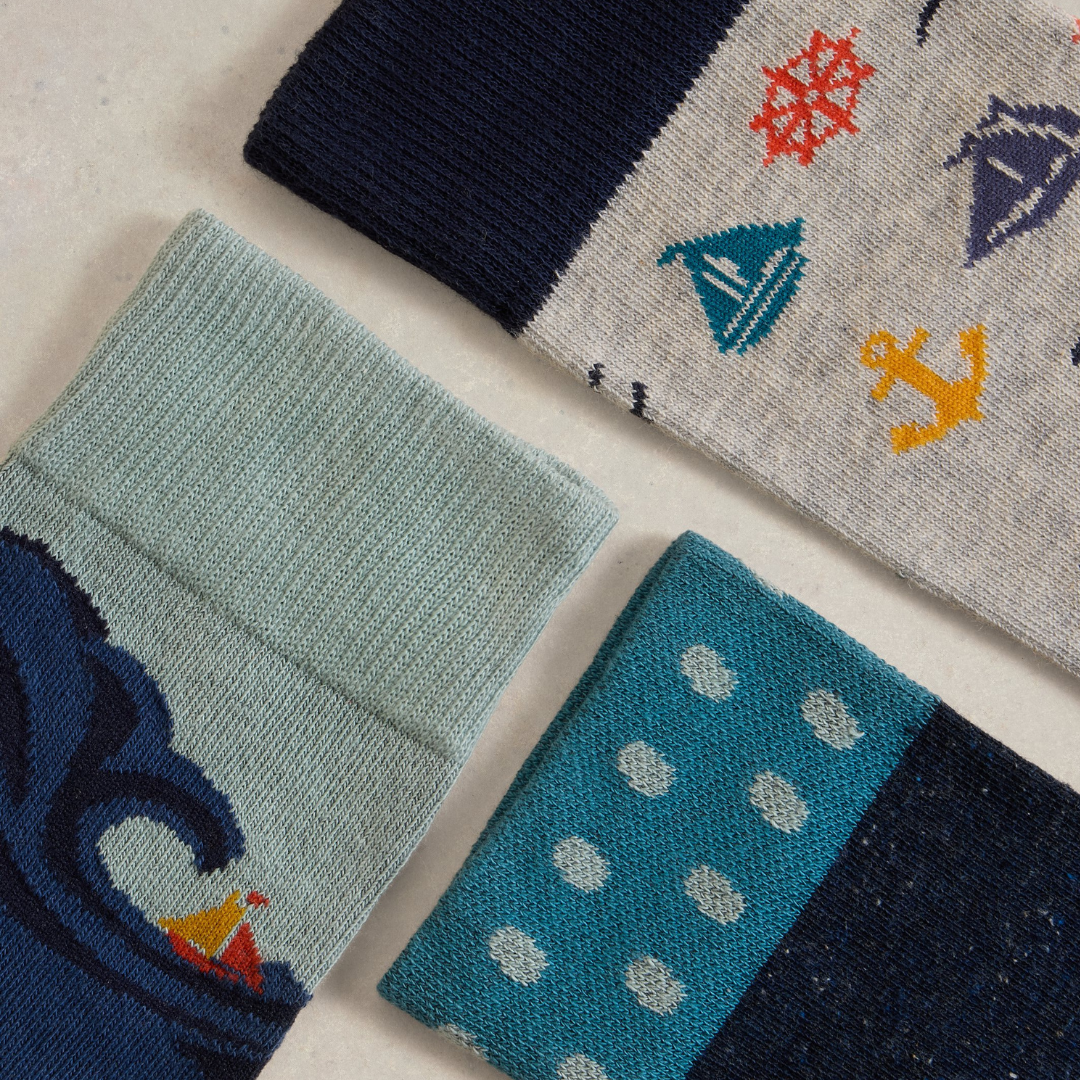 Three pairs of patterned socks: one with nautical designs, one with a wave and sailboat, and one with teal polka dots.