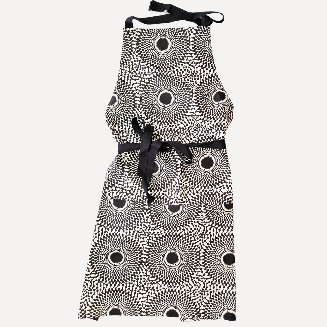 Black and white apron with a repeating sunburst pattern and black ribbon tie.