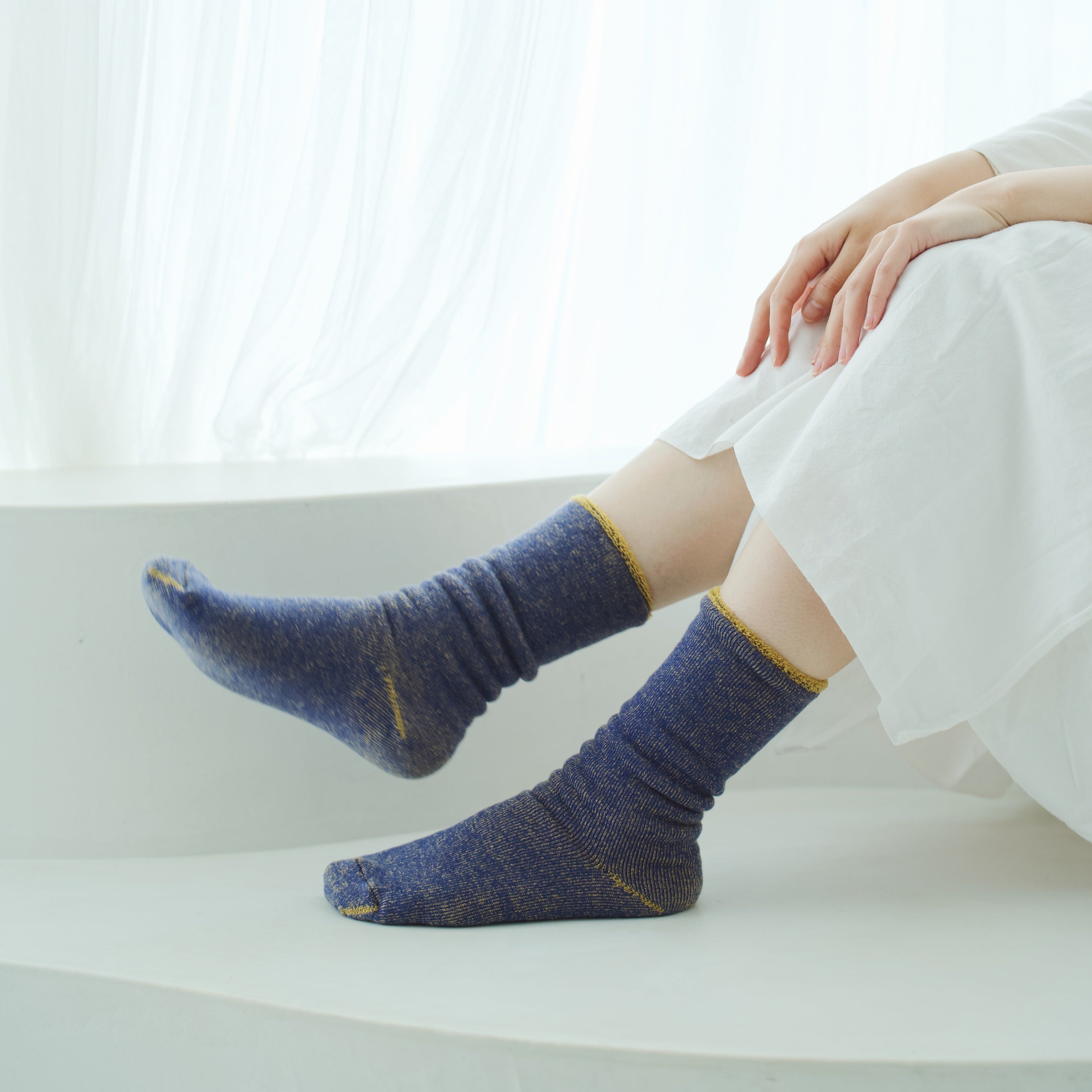 Pair of dark blue socks with gold flecks and trim.  The socks are shown on a person's legs, resting on a white surface.