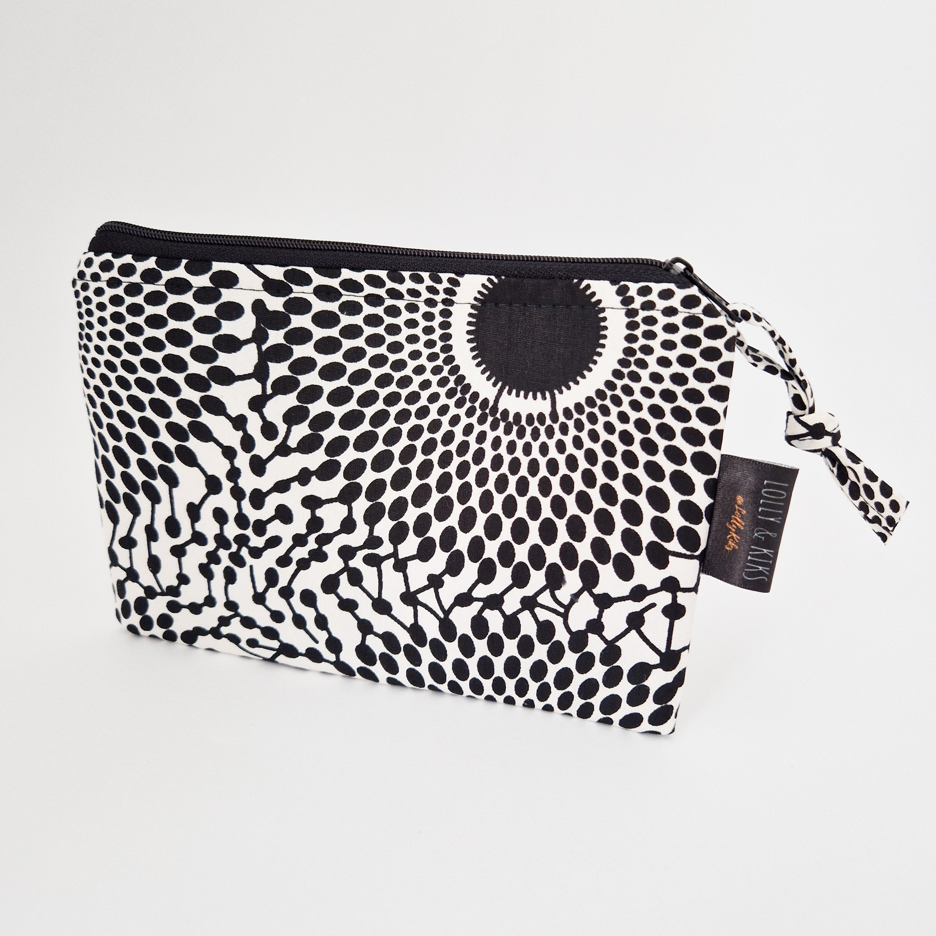 Black and white polka dot zippered pouch with a fabric pull tab.  The design features radiating circles of varying sizes.