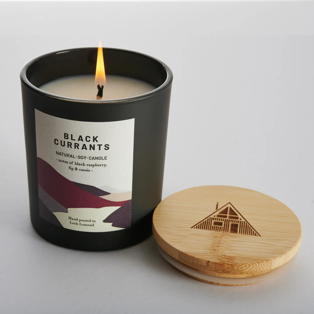 Black Currants natural soy candle in a dark gray jar with a bamboo lid.  The label features a landscape design.