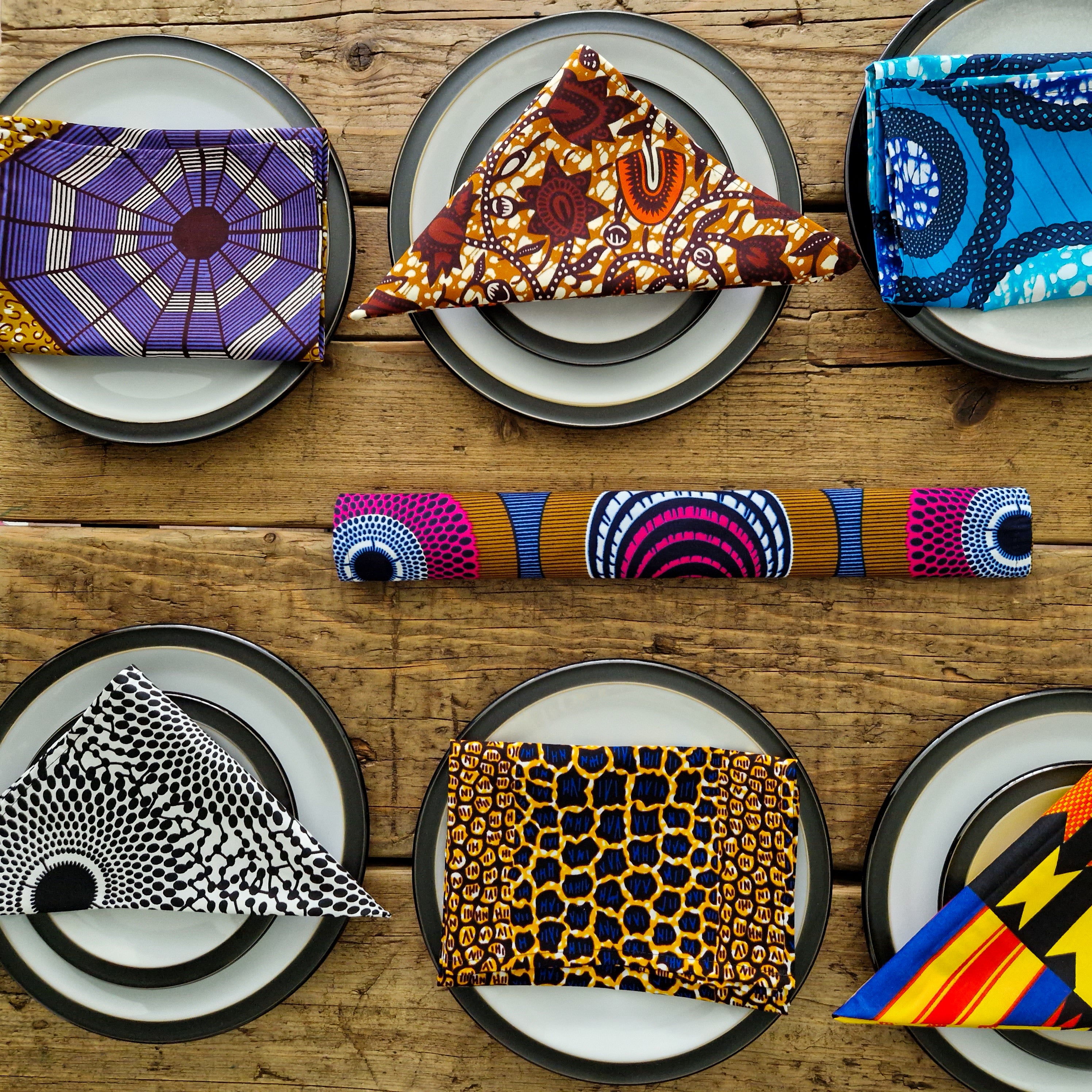 Collection of six African print fabric napkins; various vibrant colors and patterns folded on plates.