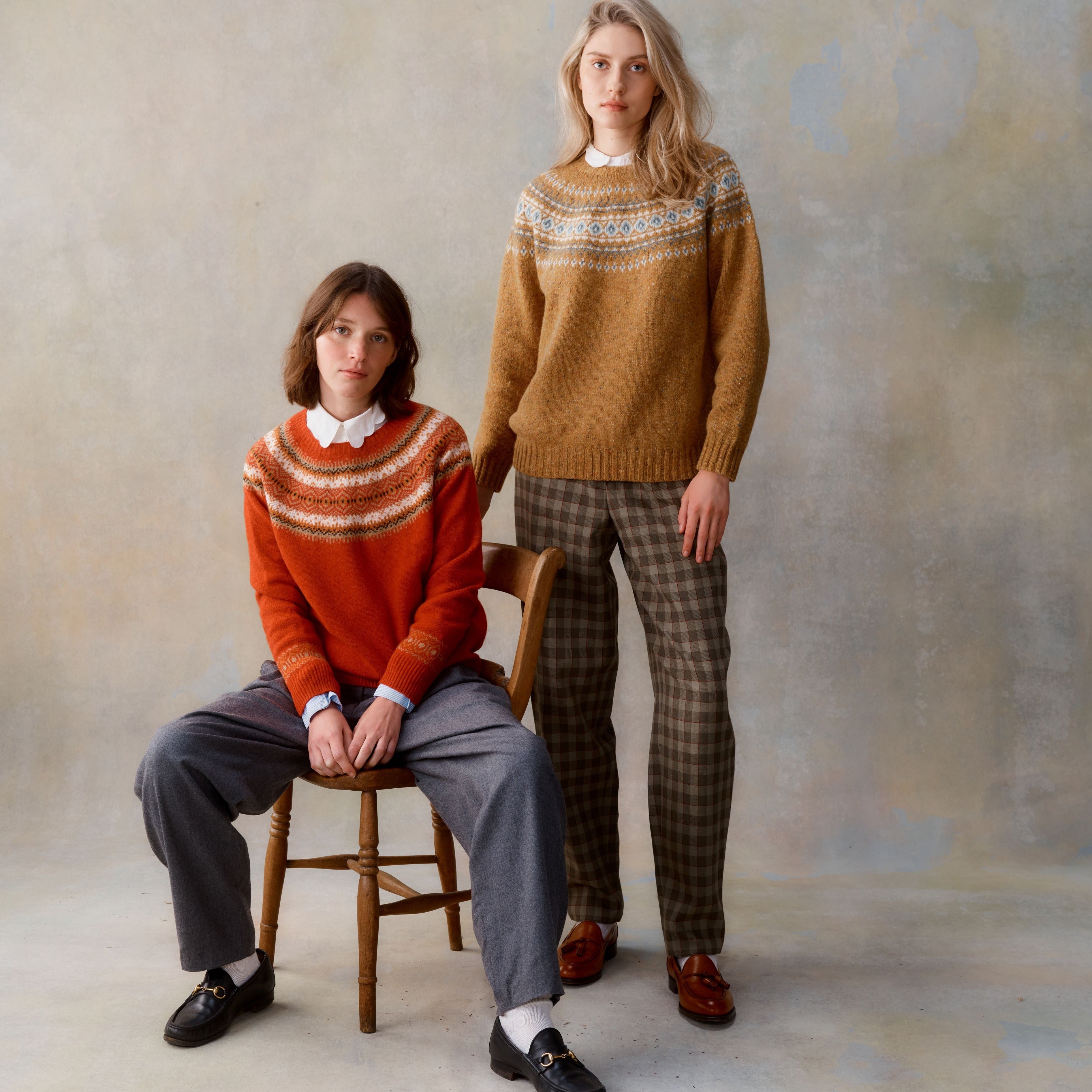 Two women model Fair Isle-patterned sweaters; one orange, one mustard yellow.