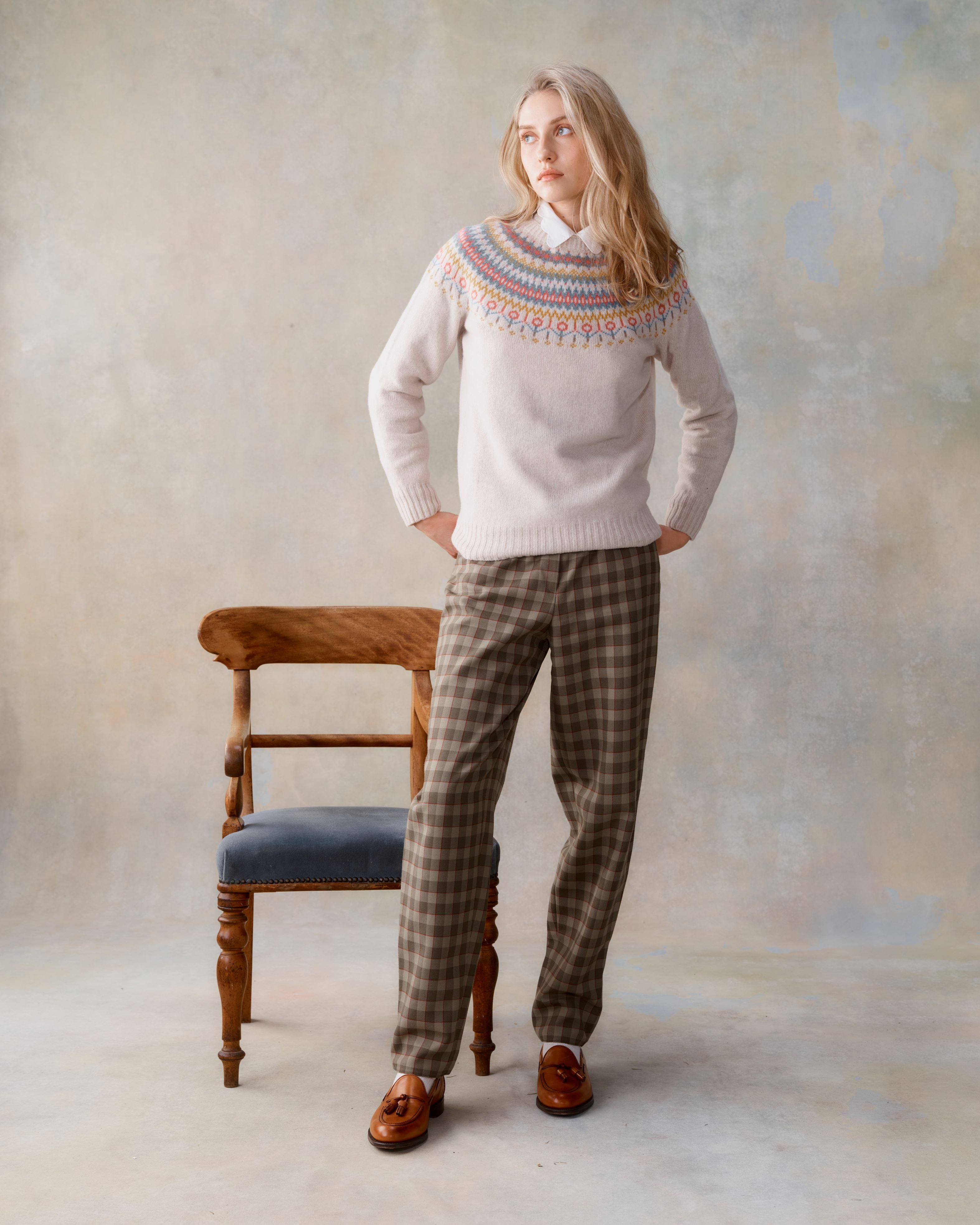 Cream Fair Isle knit sweater with a colorful Nordic-inspired pattern at the neckline, worn with brown plaid trousers and