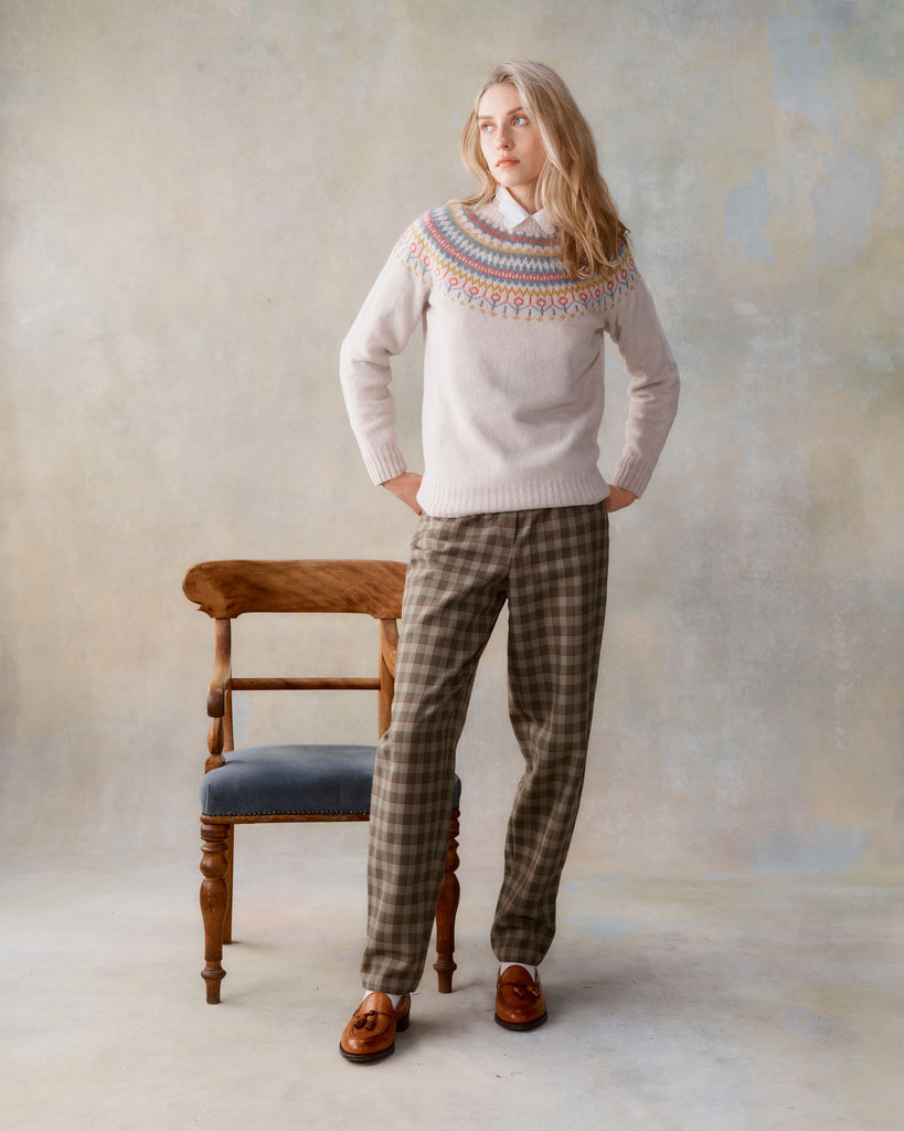 Cream Fair Isle knit sweater with a colorful Nordic-inspired pattern at the neckline, worn with brown plaid trousers and