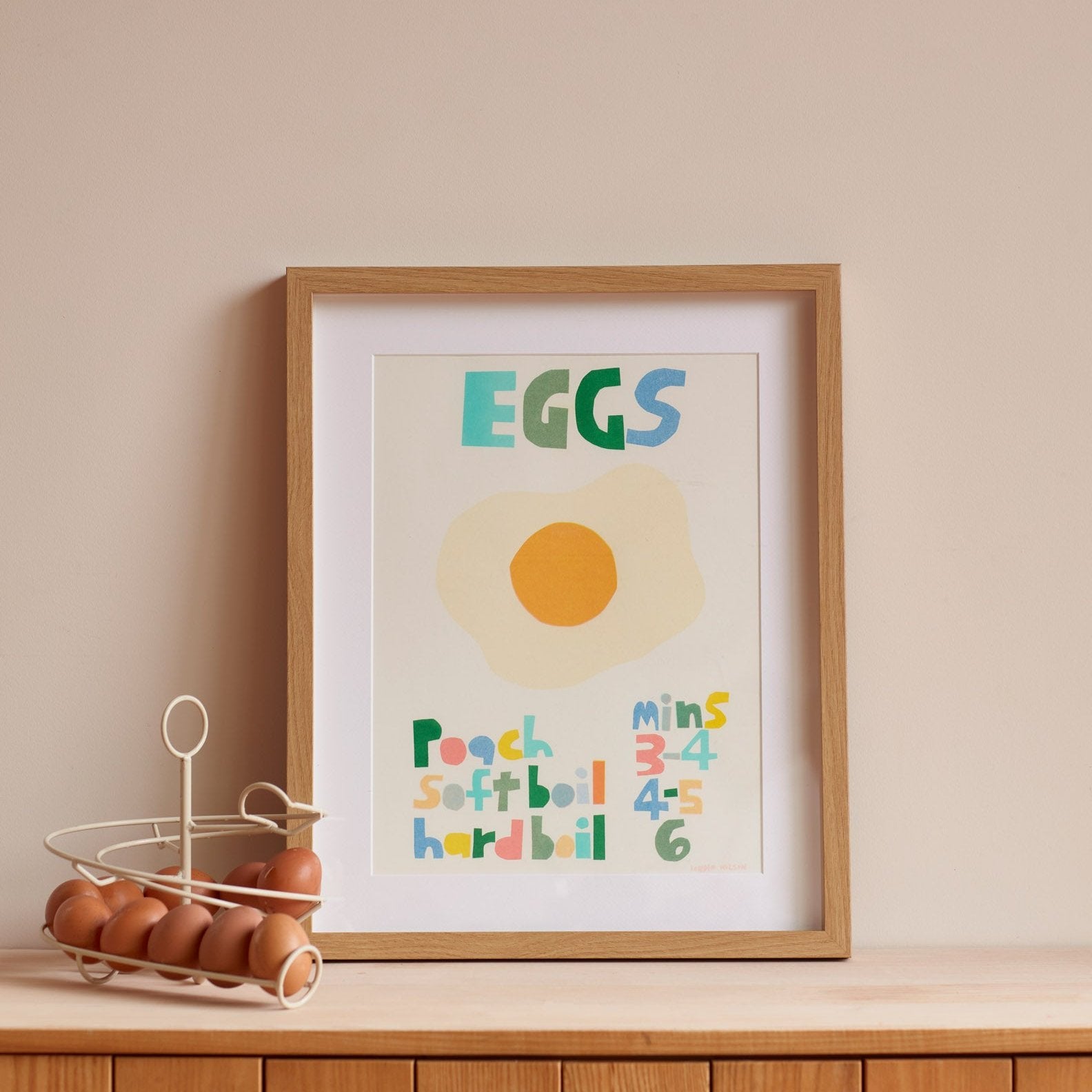 A framed art print by Donna Wilson featuring colorful text on eggs; greens, blues, oranges, and pastels.