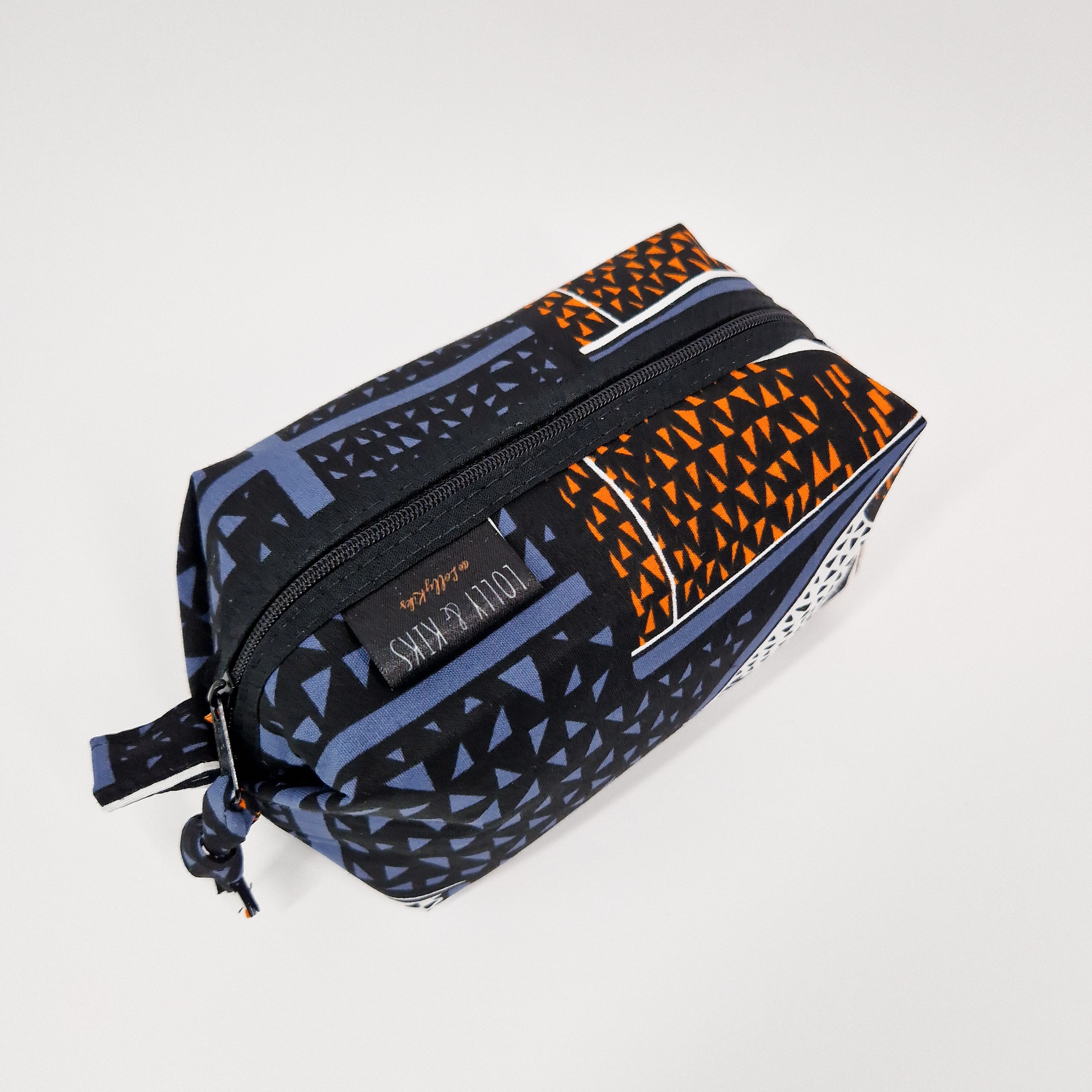 Rectangular zippered pouch with a black, orange, and blue geometric print.  The pouch has a small fabric pull tab.
