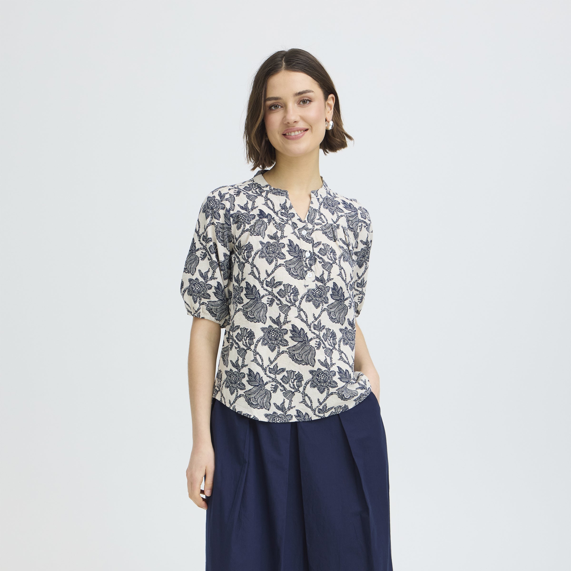 Woman wearing a floral blouse and navy pants on a light gray background