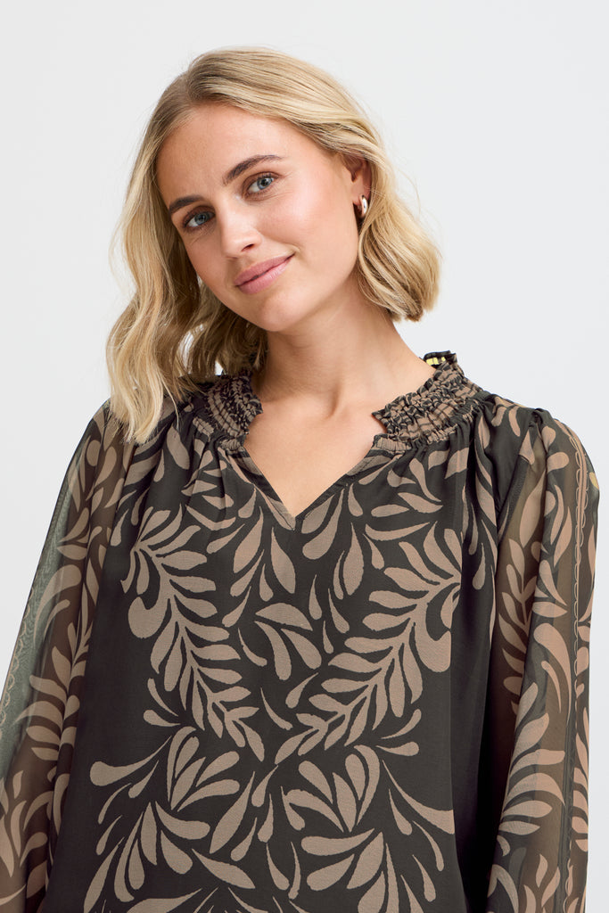 A woman wears a black and beige patterned blouse by Fransa, featuring a smocked neckline and flowing sleeves.