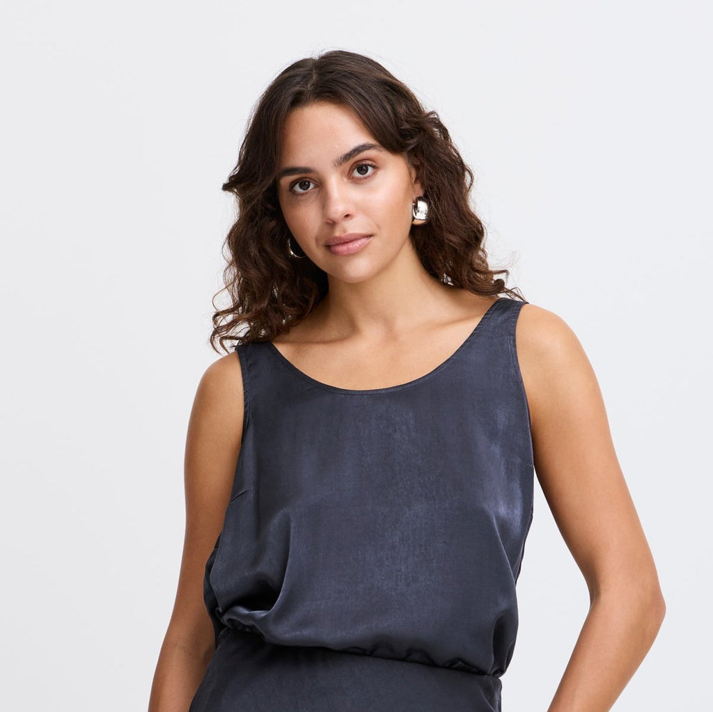 Model wearing a dark blue satin top by Fransa, styled with soft curls and silver hoop earrings.