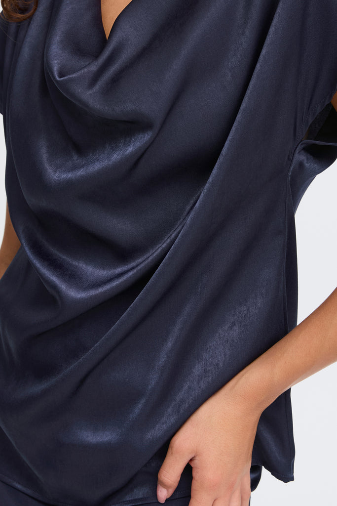 A close-up of a person wearing a navy blue draped top by Fransa, showcasing its silky texture.