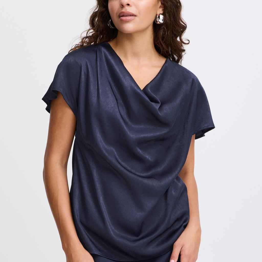 A woman in a navy blue Fransa top with a draped neckline, wearing silver hoop earrings.