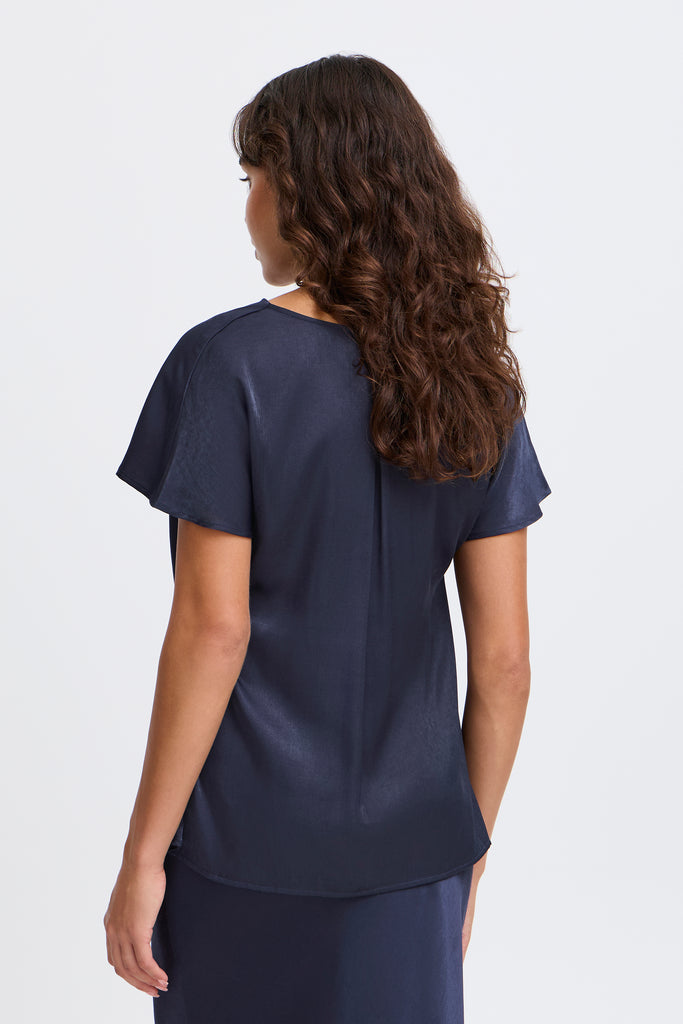 A woman with curly hair wearing a navy blue top by Fransa, viewed from behind against a light background.
