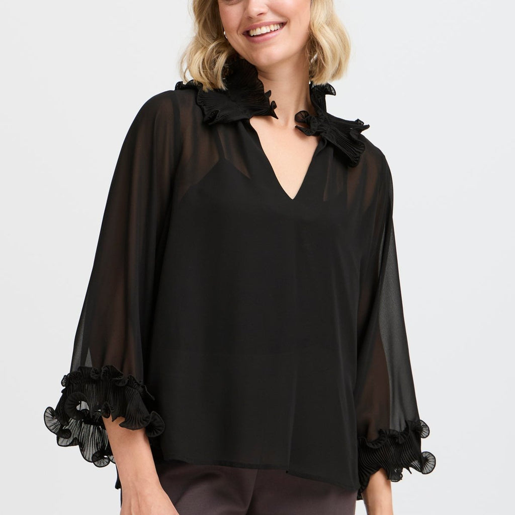 Model wearing a black Fransa blouse with ruffled sleeves and a V-neck, smiling against a light background.