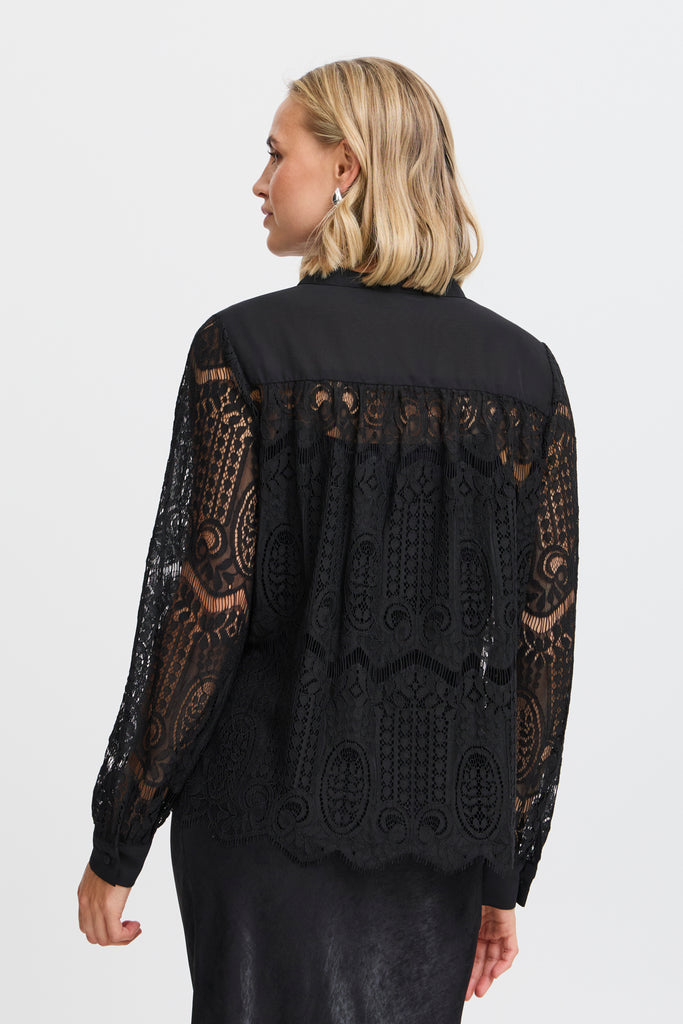 Woman with a blonde bob wearing a black lace and satin blouse by Fransa, showcasing intricate detailing from the back.