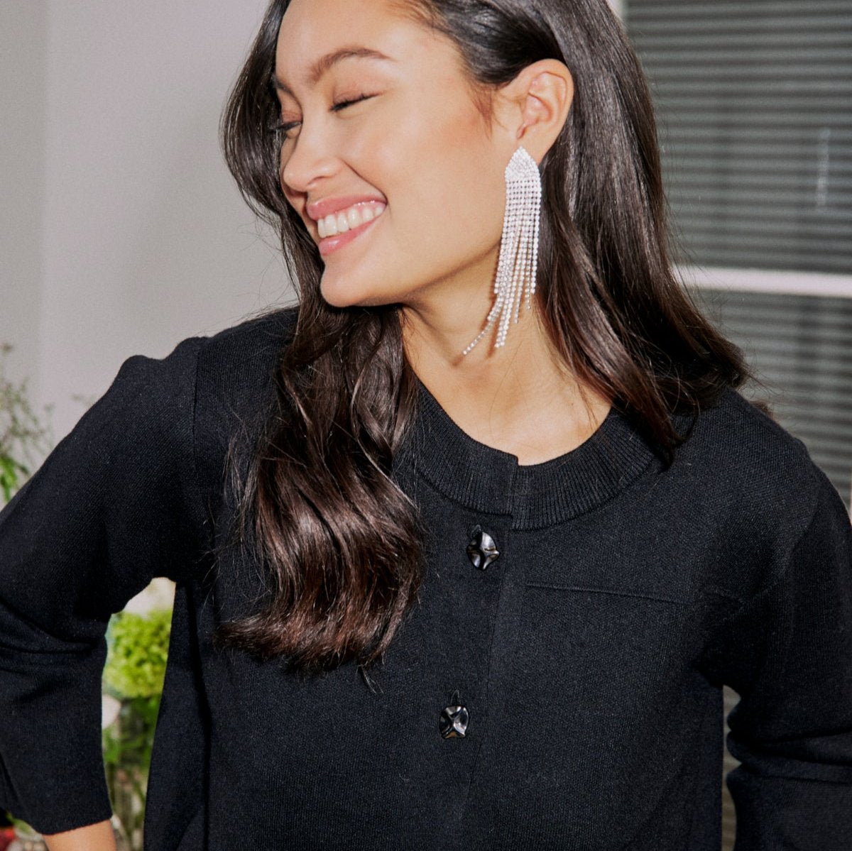 Long, crystal-encrusted drop earrings;  worn by a woman in a black cardigan.