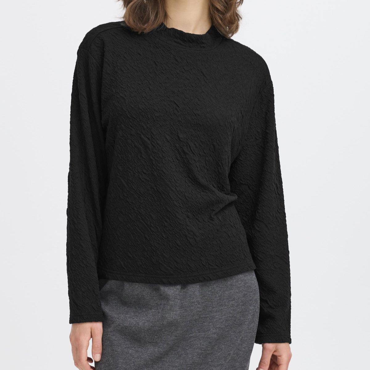 Woman wearing a black long-sleeve top and gray skirt on a white background