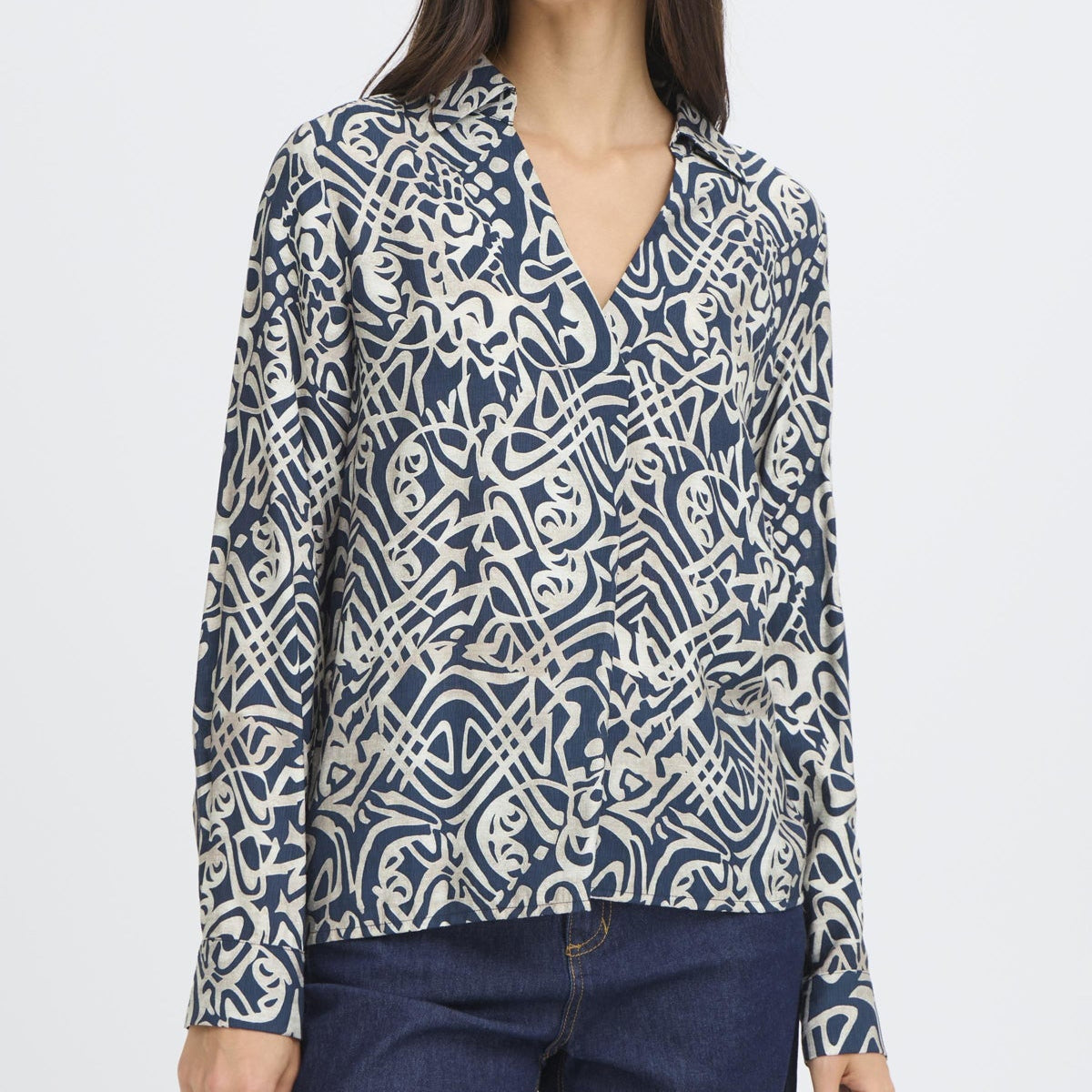 Woman wearing a patterned blouse and dark pants on a white background